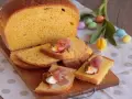 Fetta di torta al formaggio umbra ricetta originale, guarnita con uovo sodo e prosciutto crudo, su tagliere di legno, con uova colorate e tulipano.