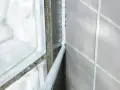 Applicator sprutar ny silikonfog längs en fog i badrummet, bredvid en duschvägg av glasblock.