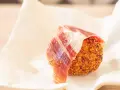 Croqueta dorada con jamón ibérico, servida sobre papel blanco.