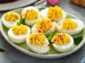 Oeufs mimosa au thon, garniture jaune crémeuse saupoudrée de paprika sur des blancs d'œufs sur une assiette verte.
