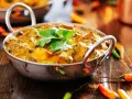 Ein cremiges Curry, garniert mit Koriander, umgeben von bunten Chilis. Ein Genuss für Liebhaber indischer Gerichte.