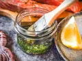 Marinade mit Kräutern und Zitrone bereit, um den Lachs zu verfeinern. Ein Pinsel liegt in der Glasflasche.
