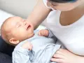 Płaczący noworodek w ramionach mamy. Szukamy odpowiedzi, co na kolki u noworodka, by ulżyć maluszkowi.