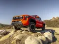 Pomarańczowy Toyota pickup pokonuje kamienisty teren na tle wzgórz.