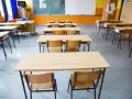 Pusta klasa szkolna z rzędami ławek i krzeseł. W tle tablica i okna. Obowiązek nauki czeka na uczniów.