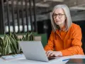 Mujer mayor con cabello plateado y gafas trabajando en su laptop, un ejemplo de jubilación activa.