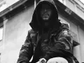 Mężczyzna w kapturze i kurtce moro, z widocznym logo Timberland. Jego styl to ćpaj stajl czlonkowie, gotowy na miejskie wyzwania.