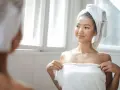 Mujer con toalla en la cabeza y el cuerpo, sonriendo ante el espejo. Un consejo para saber como quitar la pelusa de las toallas nuevas.