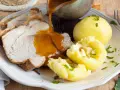 Omas Sonntagsessen: Saftiger Schweinebraten mit knuspriger Kruste, Klößen und Rotkohl, übergossen mit dunkler Soße.