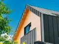 Nowoczesny dom z drewnianą i grafitową elewacją z blachy, pod błękitnym niebem.