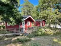 Röda stugor med träaltaner och ramper på Waxholms camping, omgivna av grönska och träd.