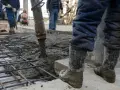 Beton wylewany na zbrojenie. Pracownicy w gumowcach nadzorują proces, który decyduje, ile kosztują fundamenty.
