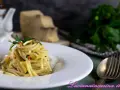 Un piatto di spaghetti alla carrettiera, conditi con aglio, olio, peperoncino e prezzemolo, con pecorino grattugiato sullo sfondo.