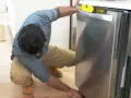 Man leveling a stainless steel dishwasher with a yellow bubble level, part of a guide on how to replace a dishwasher.