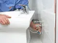Instalator podłącza wężyki do nowego, białego bidetu.