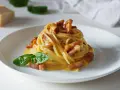 Pyszna carbonara z makaronem spaghetti, boczkiem i bazylią. W tle widać kawałek parmezanu, sugerując autentyczne carbonara skladniki.