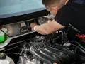 Mechanik naprawia silnik, prawdopodobnie usuwając uciążliwy błąd P0011. Widać zbiornik płynu i elementy silnika.