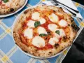 Pyszna pizza napolitana z pomidorami, mozzarellą i bazylią na niebieskim obrusie.