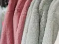 Des vêtements douillets en matière molleton, aux couleurs rose et vert d'eau, sont suspendus sur des cintres.