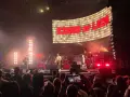 Koncert Kings of Leon na żywo. W tle wielki ekran z napisem "KINGS OF LEON", na scenie zespół gra dla rozentuzjazmowanej publiczności.