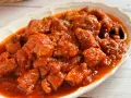 Plato de magro con tomate, trozos de carne tierna en una salsa roja y sabrosa, servido en una fuente blanca.
