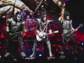 Les membres du groupe de rock Kiss, maquillés et costumés, jouent sur scène. Un chanteur lève un bras en signe de victoire.