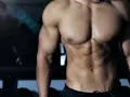 Muskulös man med synliga magmuskler i gym. En spegelbild av en annan person syns i bakgrunden. Frågan "hur deffar man" kan besvaras med denna fysik.