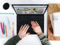 Hände tippen auf einem Laptop, daneben ein Kalender und eine Kaffeetasse.