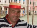 Un gondoliere sorridente, con il suo cappello iconico, pronto a navigare i canali di Venezia, la città che porta il soprannome di "La Serenissima".