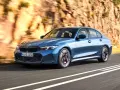 Niebieskie BMW klasy średniej jedzie po krętej drodze w skalistym krajobrazie.