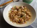 Pyszne ciasto wonton polane pikantnym sosem, posypane szczypiorkiem i sezamem. Obok pałeczki i miseczka z sosem.