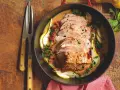 Lonza di maiale in padella morbida, affettata e servita con pere, salsa cremosa e prezzemolo tritato.