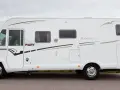 Vit husbil, Pilote G740 Aventura, parkerad vid en väg med gräs och träd i bakgrunden.