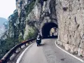 Motocykliści przemierzają malowniczą strada della forra, wjeżdżając w skalny tunel. Widok na jezioro i góry zapiera dech.
