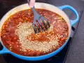 Eine Person rührt Linsen in eine köchelnde Bolognese-Sauce in einem blauen Topf.