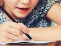 Dziecko zmagające się z pisaniem, co może być oznaką dysleksji. Skupienie na twarzy i ręce trzymającej ołówek.