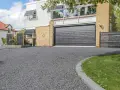En vacker uppfart med mörkt grus leder fram till ett modernt hus med garageport.