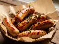 Saftige bratwurst im airfryer, goldbraun und mit Rosmarin garniert, serviert in einer Holzschale auf rustikalem Untergrund.