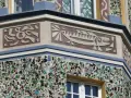 Sgraffito na fasadzie budynku: stylizowana ryba i abstrakcyjne wzory. Dolna część ozdobiona mozaiką z kolorowego szkła.