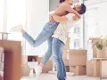 Glückliches Paar umarmt sich in einem neuen Zuhause voller Umzugskartons. Ein aufregender Moment, wann zusammenziehen!
