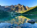 Morskie Oko jesienią. Lśniąca tafla jeziora odbija skaliste szczyty Tatr i zielone lasy.