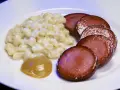 Stuvade makaroner snabbt vis med skivad falukorv och en klick senap på en vit tallrik.