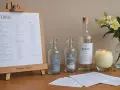 Planowanie wesela: ile wódki na wesele? Na stole butelki, świeca i bukiet kwiatów, obok lista gości i menu.