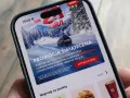 Aplikacja ORLEN z promocją na paliwo za punkty. Zima, góry i samochód na ekranie telefonu.