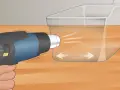 A heat gun is used on low setting to gently warm a scratched plexiglass surface, showing how to get scratches out of plexiglass.
