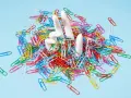 White hands emerge from a pile of colorful paperclips, symbolizing the struggle of how to stop being a workaholic and escape the daily grind.