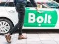 Chcesz wiedzieć, jak zostać kierowcą Bolta? Mężczyzna otwiera drzwi białego samochodu z zielonym logo Bolt.