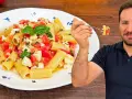 Un uomo sorride mentre assaggia una forchettata di pasta alla checca, un piatto fresco con pomodori, mozzarella e basilico.