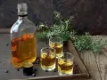 Flasche mit bernsteinfarbenem Gin, drei Gläser und Wacholderzweige. Perfekt für Gin DIY.