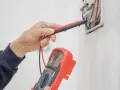 Elektryk sprawdza instalację elektryczną multimetrem, przygotowując protokół odbioru.